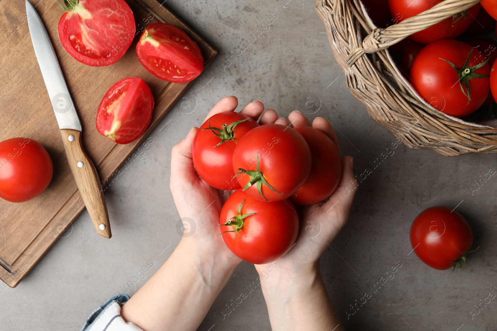 Photo of Woman with ripe tomatoes at grey table, top view