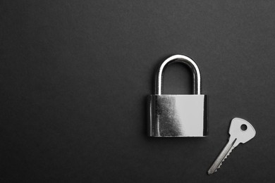 Modern padlock and key on black background, flat lay. Space for text