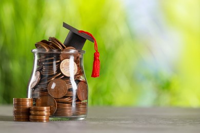 Photo of Scholarship concept. Graduation cap and jar with coins on grey table against blurred background, space for text