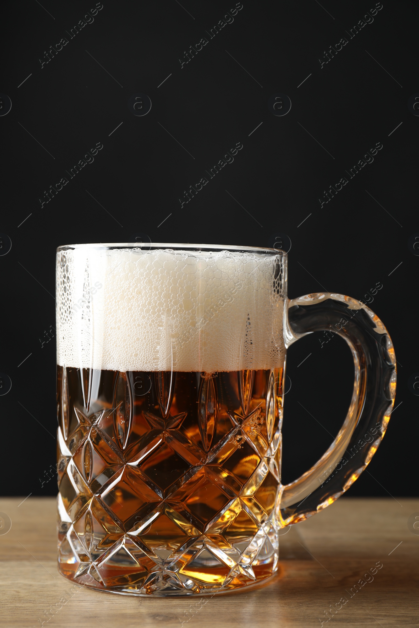 Photo of Mug with fresh beer on wooden table against black background