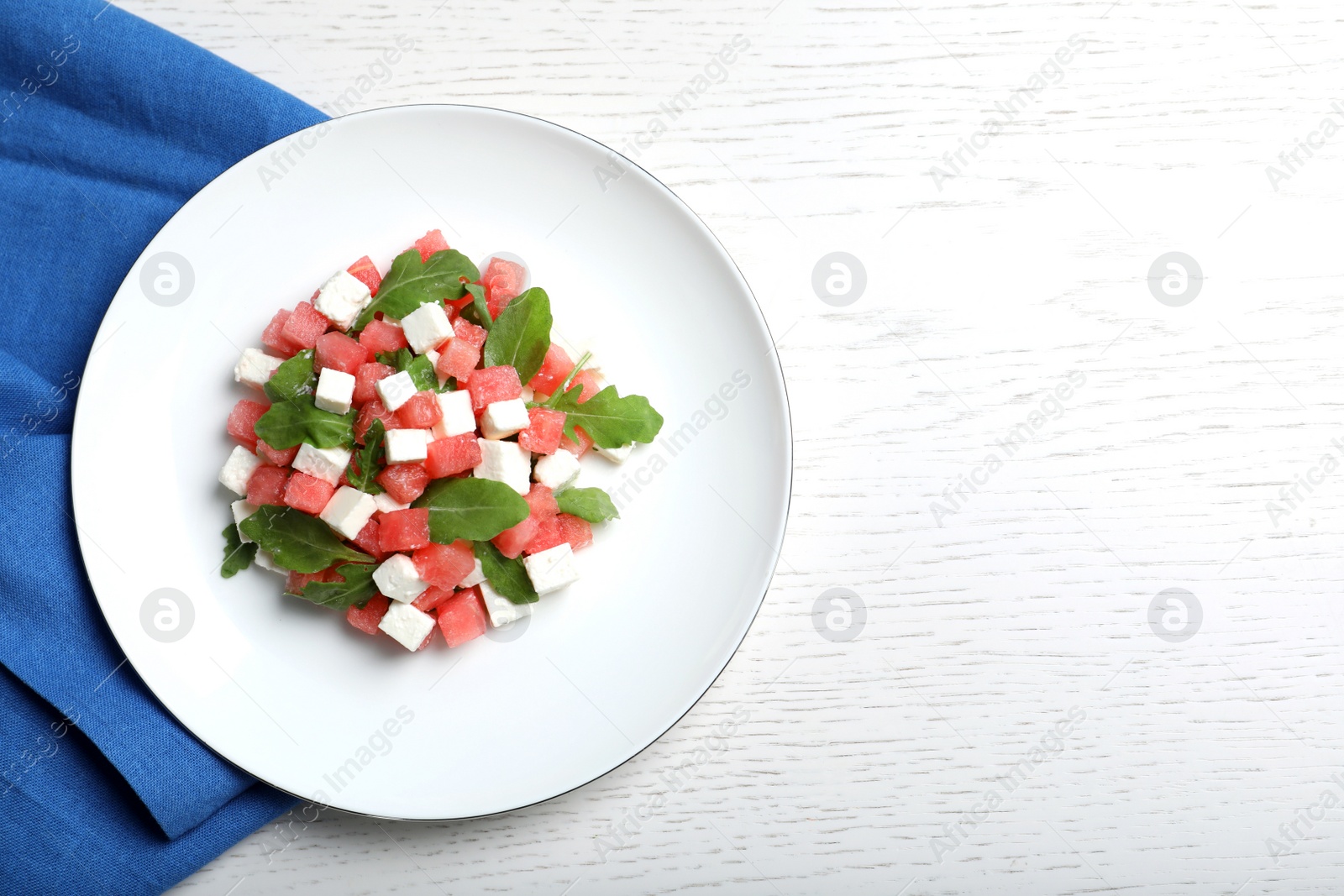 Photo of Delicious salad with watermelon, arugula and feta cheese on white wooden table, flat lay. Space for text