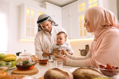 Photo of Happy Muslim family with little son at served table in kitchen