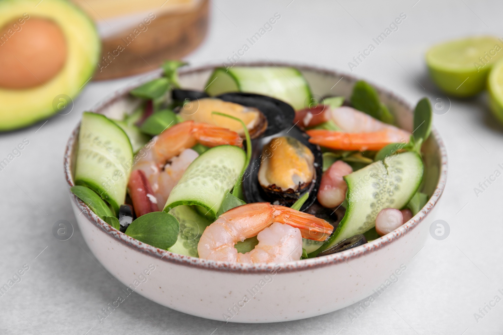 Photo of Bowl of delicious salad with seafood on light grey table, closeup