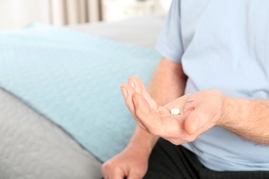 Photo of Senior man holding pill indoors, closeup. Space for text