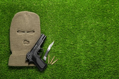 Photo of Flat lay composition with balaclava and weapons on green grass. Space for text