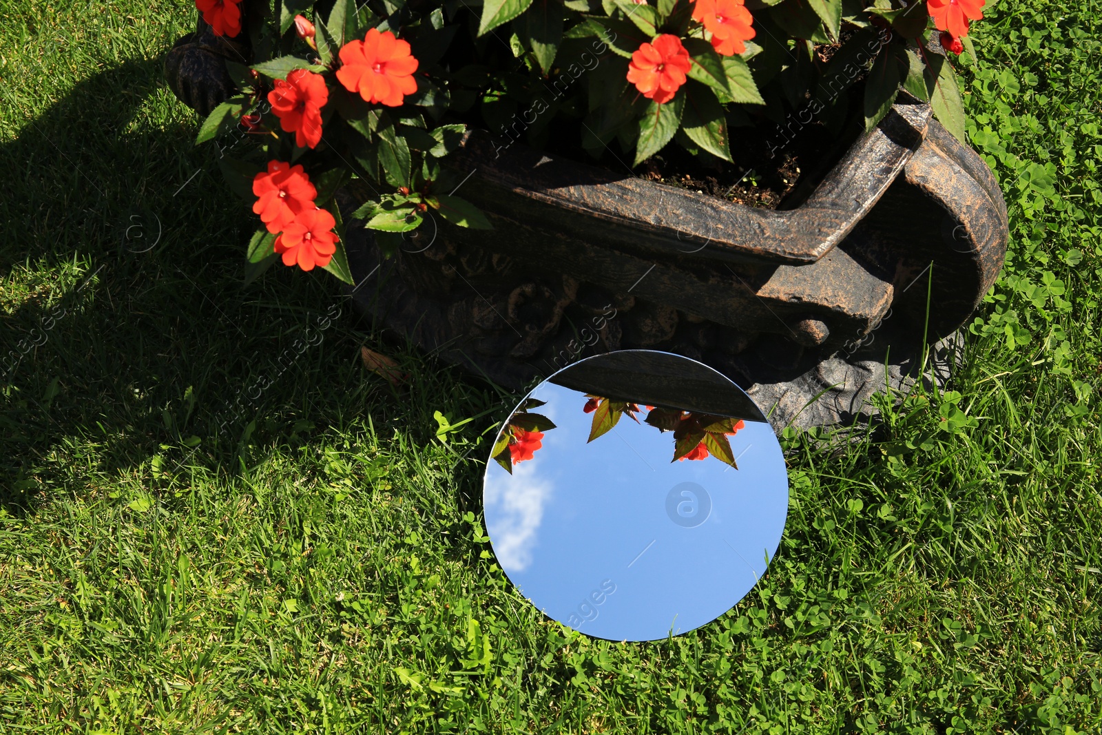 Photo of Round mirror on green grass reflecting sky and beautiful flowers