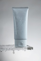 Moisturizing cream in tube on glass with water drops against grey background