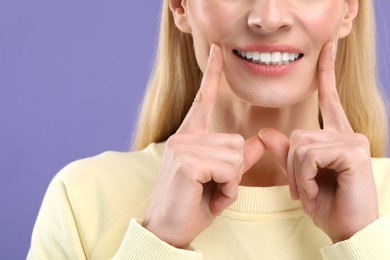 Photo of Woman showing her clean teeth and smiling on violet background, closeup