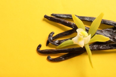 Vanilla pods and beautiful flower on yellow background, closeup. Space for text