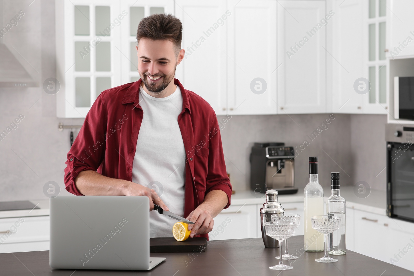 Photo of Man learning to make cocktail with online video on laptop at table in kitchen. Time for hobby