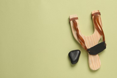 Photo of Wooden slingshot with pebble on olive background, top view. Space for text