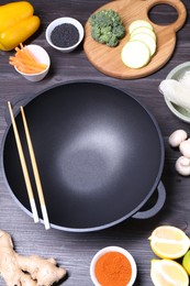 Photo of Empty iron wok, chopsticks and ingredients on dark grey wooden table, above view