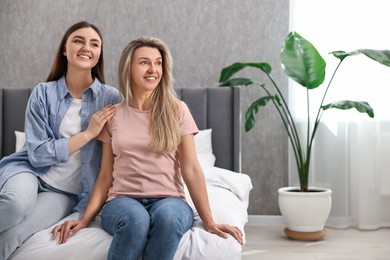 Happy young women sitting on bed at home, space for text