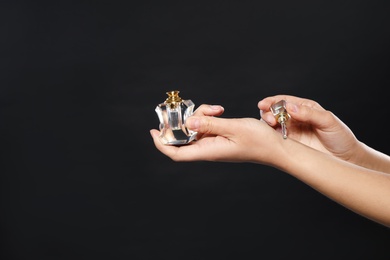 Photo of Young woman applying perfume on wrist against black background, closeup