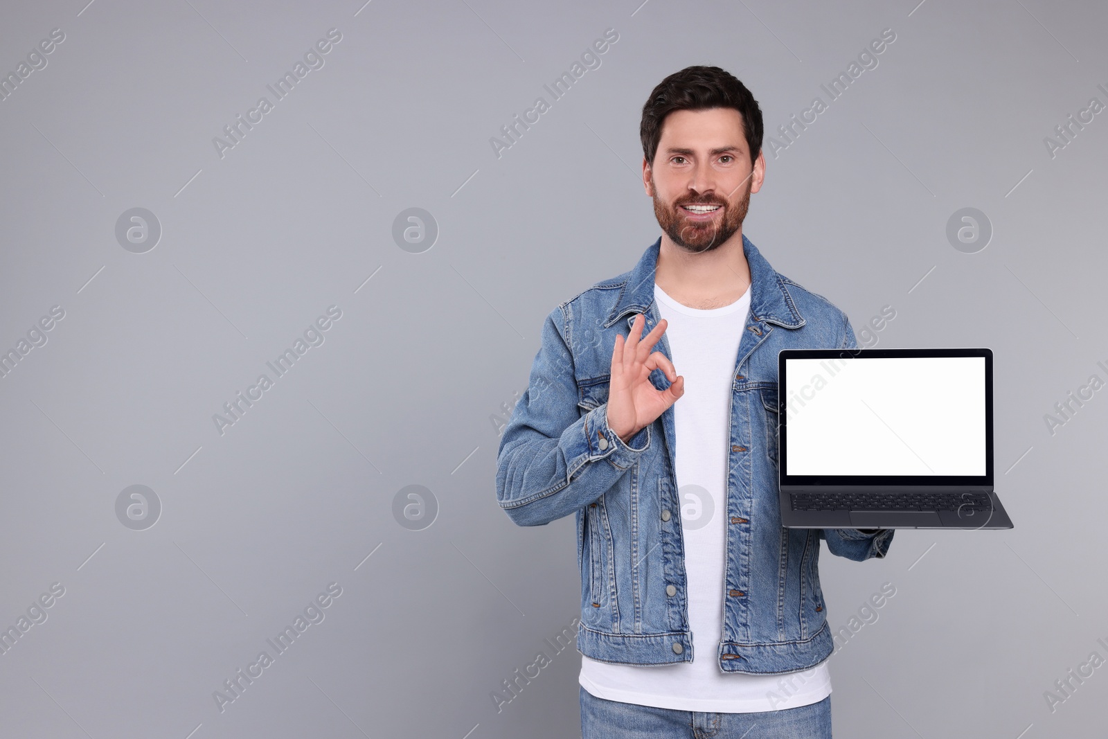 Photo of Happy man with laptop showing ok gesture on light grey background. Space for text