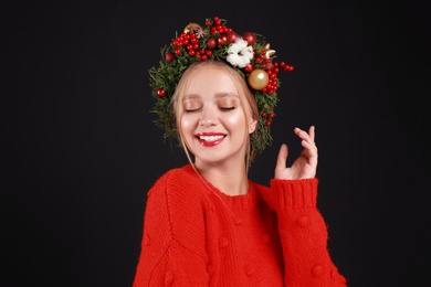 Photo of Beautiful young woman wearing Christmas wreath on black background