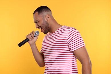 Photo of Handsome man with microphone singing on orange background