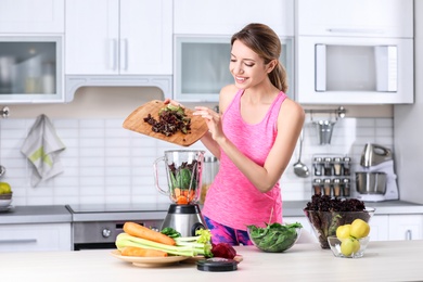 Young woman preparing tasty healthy smoothie at table in kitchen