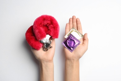 Woman with furry handcuffs and condoms on white background, top view. Sex game