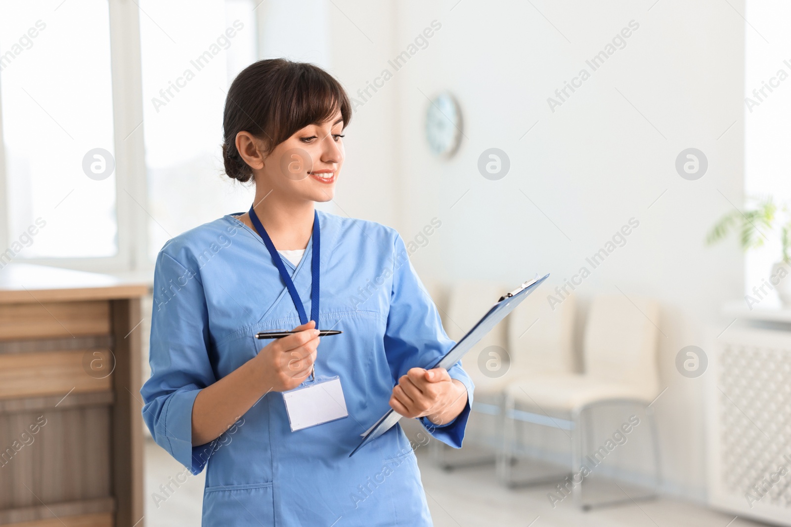 Photo of Portrait of smiling medical assistant with clipboard in hospital. Space for text