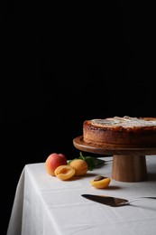Tasty apricot pie with powdered sugar on table against black background, space for text