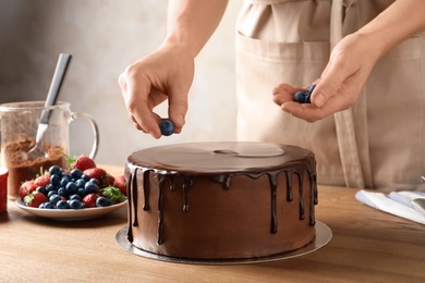 Photo of Baker decorating fresh delicious homemade chocolate cake with berries on table, closeup