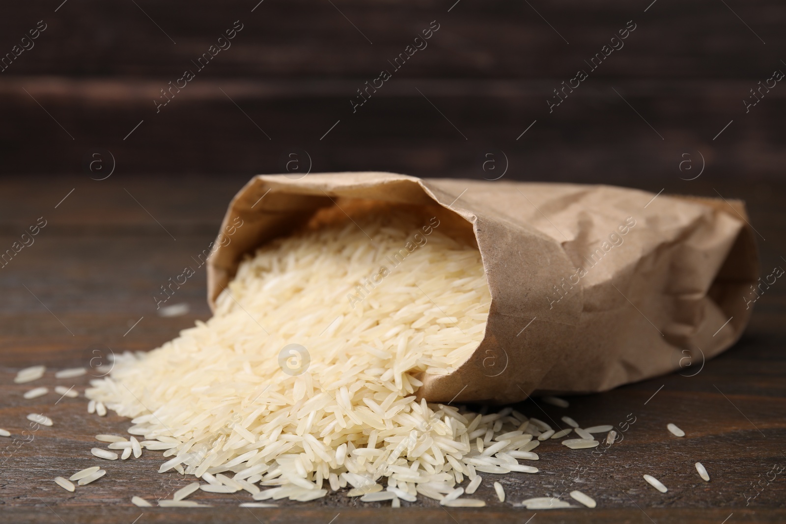Photo of Overturned paper bag with raw rice on wooden table, closeup