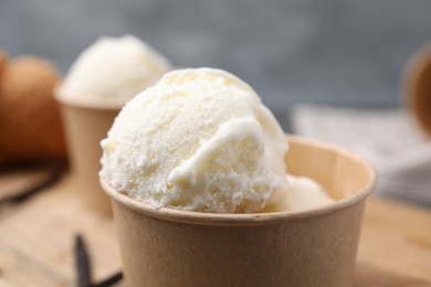 Photo of Paper cups with delicious ice cream and vanilla pods on wooden board, closeup