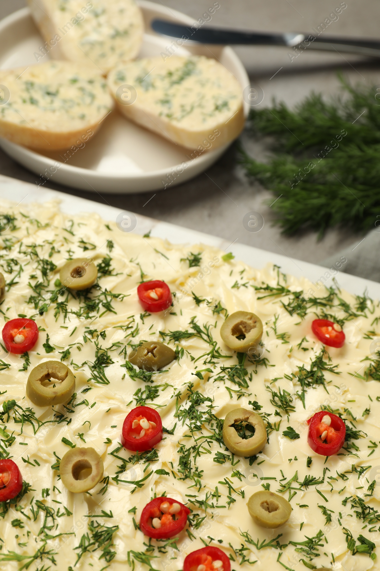 Photo of Fresh butter board with cut olives, dill and pepper on grey table, closeup