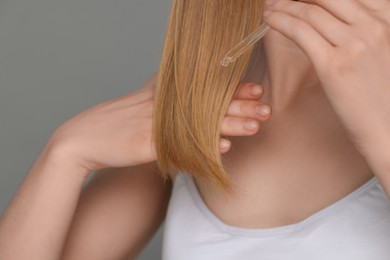 Woman applying essential oil onto hair on grey background, closeup