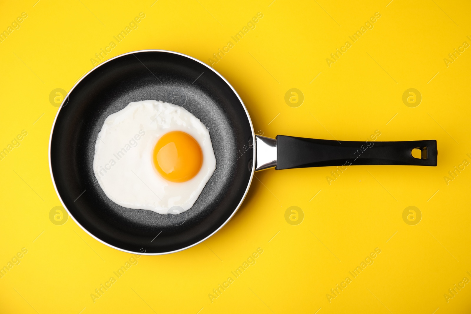 Photo of Tasty fried egg in pan on yellow background, top view