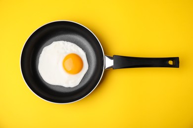 Photo of Tasty fried egg in pan on yellow background, top view