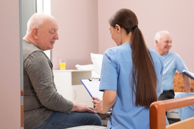 Photo of Nurse talking with senior patient in hospital ward. Medical assisting