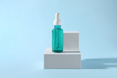 Photo of Presentation of bottle with cosmetic serum on light blue background