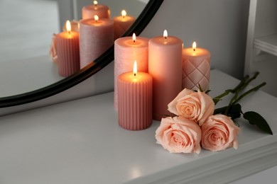 Burning candles and roses on white console table near mirror, space for text
