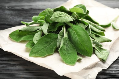 Photo of Bunch of fresh sage leaves on black wooden table, closeup