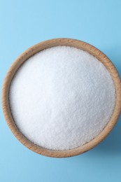 Photo of Organic white salt in bowl on light blue background, top view