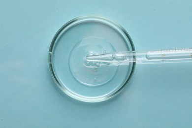 Glass pipette and petri dish with liquid on light blue background, top view