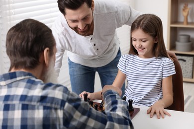 Photo of Family playing chess together at table in room