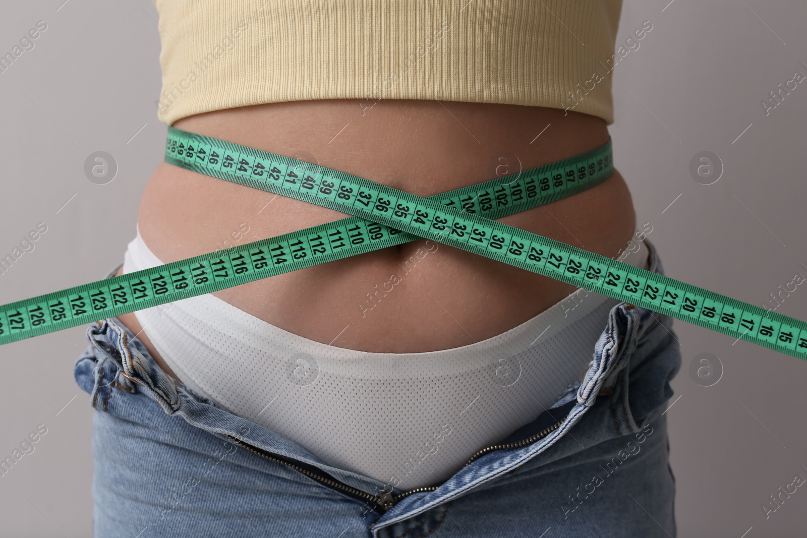 Photo of Woman in unfit jeans with measuring tape on light grey background, closeup