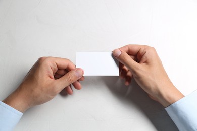 Man holding blank card at white table, top view. Mockup for design