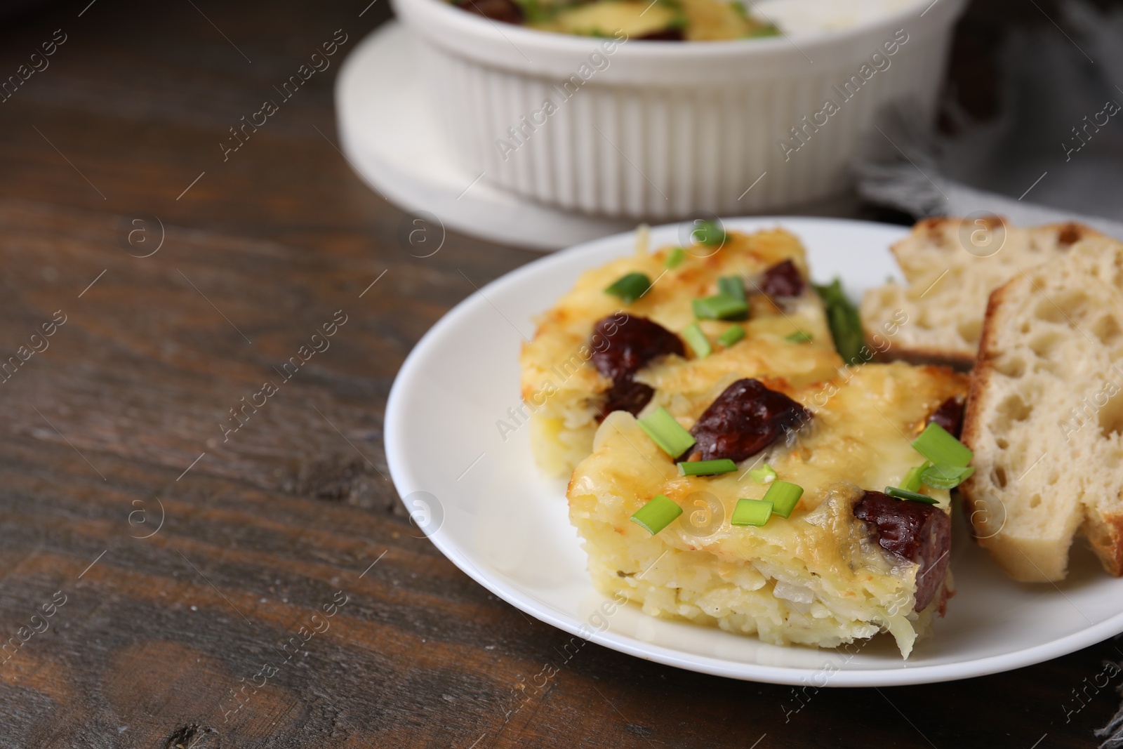 Photo of Tasty sausage casserole with green onion and bread on wooden table, closeup. Space for text