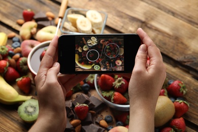 Blogger taking picture of chocolate and fruits at table, top view