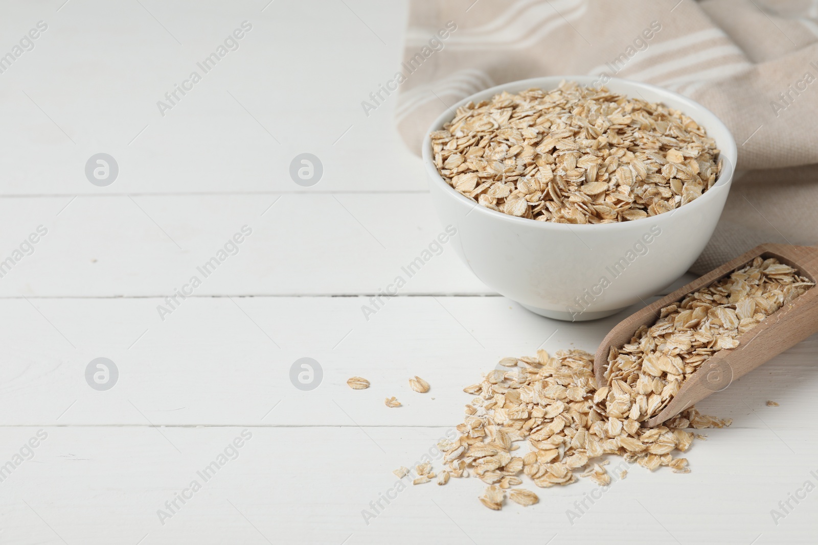 Photo of Bowl and scoop with oatmeal on white wooden table, space for text