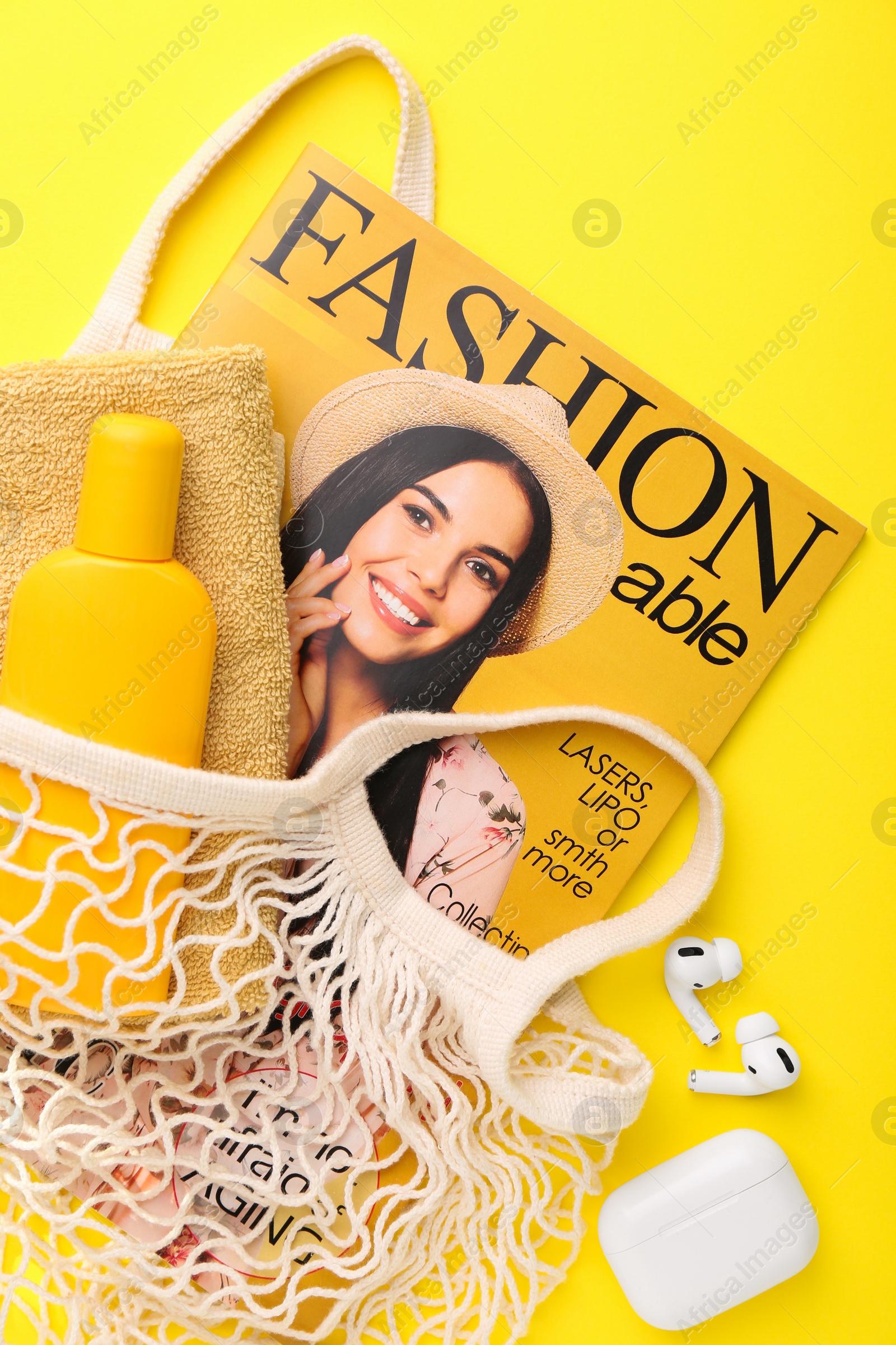 Photo of String bag with fashion magazine and beach accessories on yellow background, flat lay