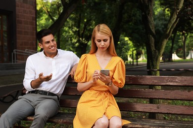 Photo of Young woman with smartphone ignoring her boyfriend in park. Boring date