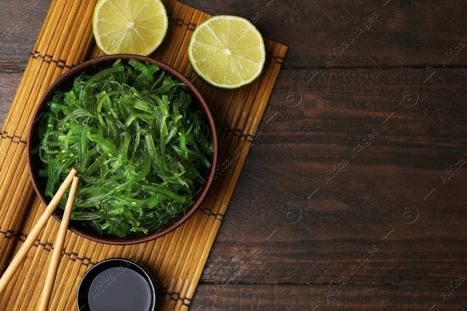 Photo of Tasty seaweed salad in bowl served on wooden table, flat lay. Space for text