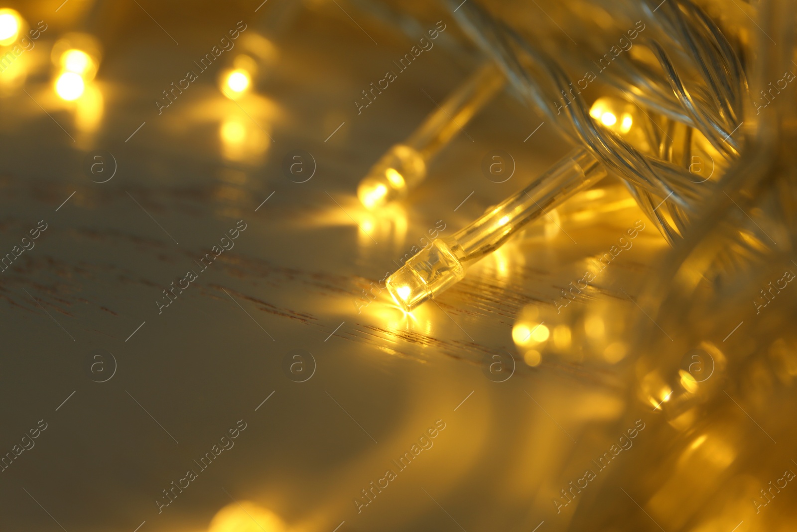 Photo of Glowing Christmas lights on white wooden background, closeup