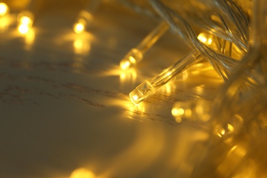 Photo of Glowing Christmas lights on white wooden background, closeup