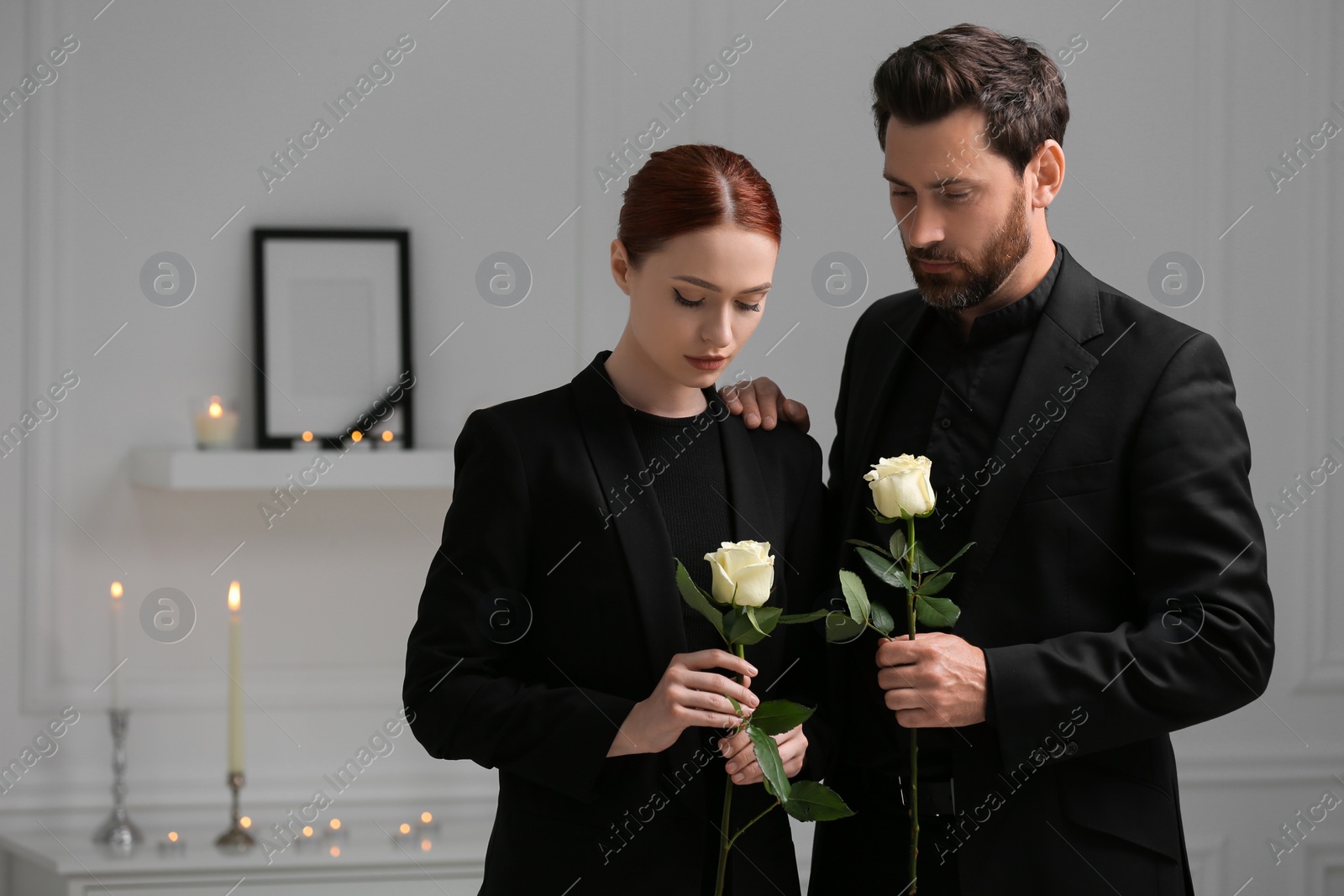 Photo of Sad couple with white roses mourning indoors. Funeral ceremony